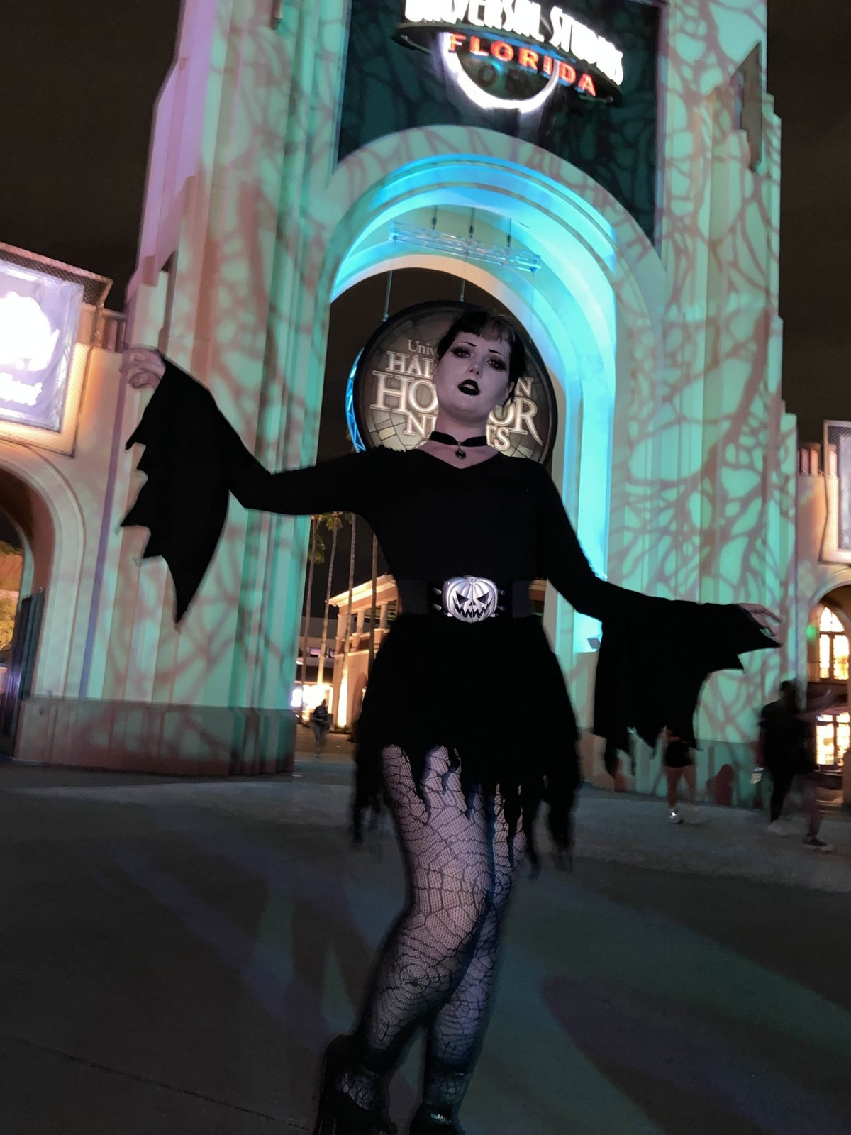 Ren wearing the silver-tone pumpkin buckle belt over a black bat-sleeve dress outside Universal Studios at night