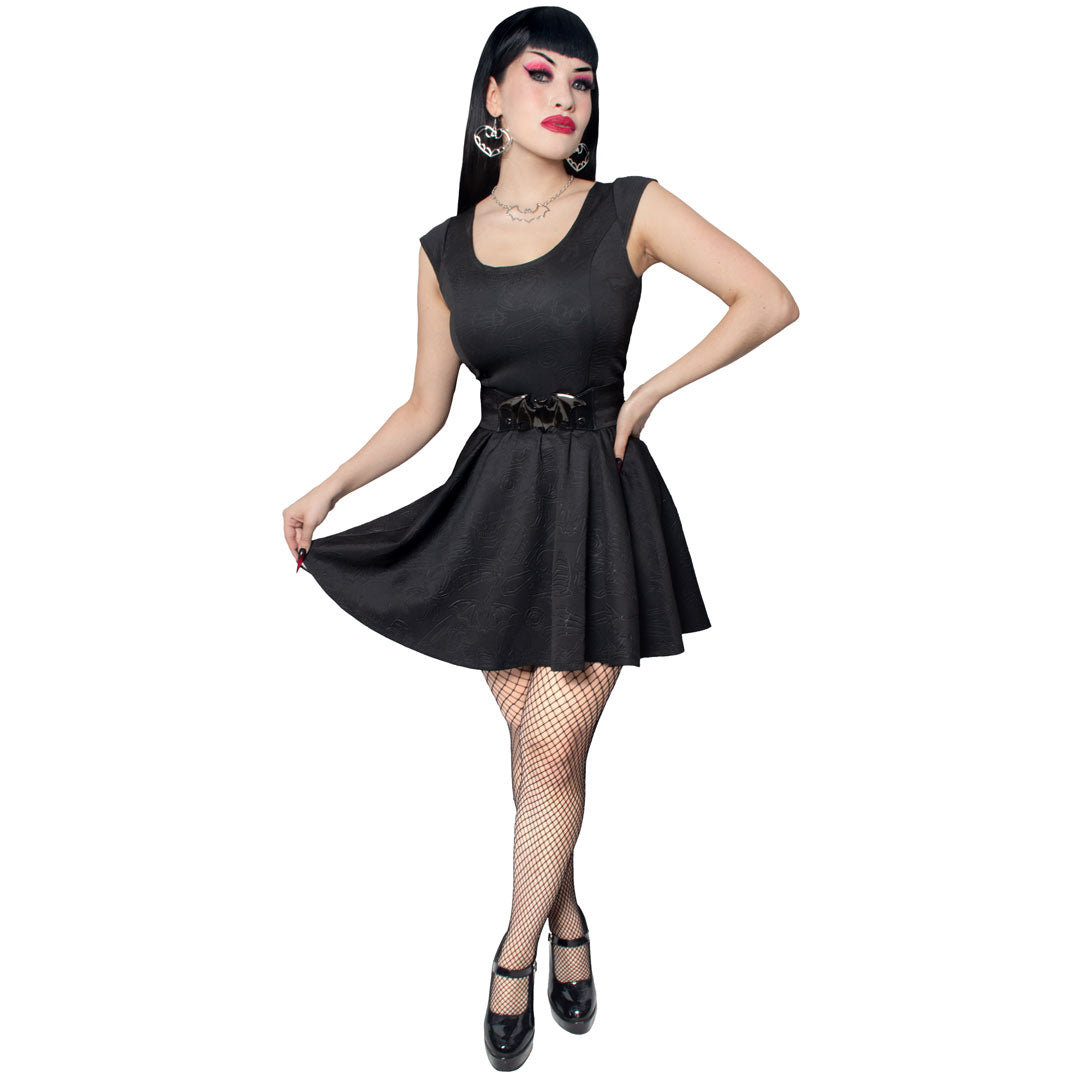 Woman wearing a black sleeveless gothic skater dress with a belt on a white background
