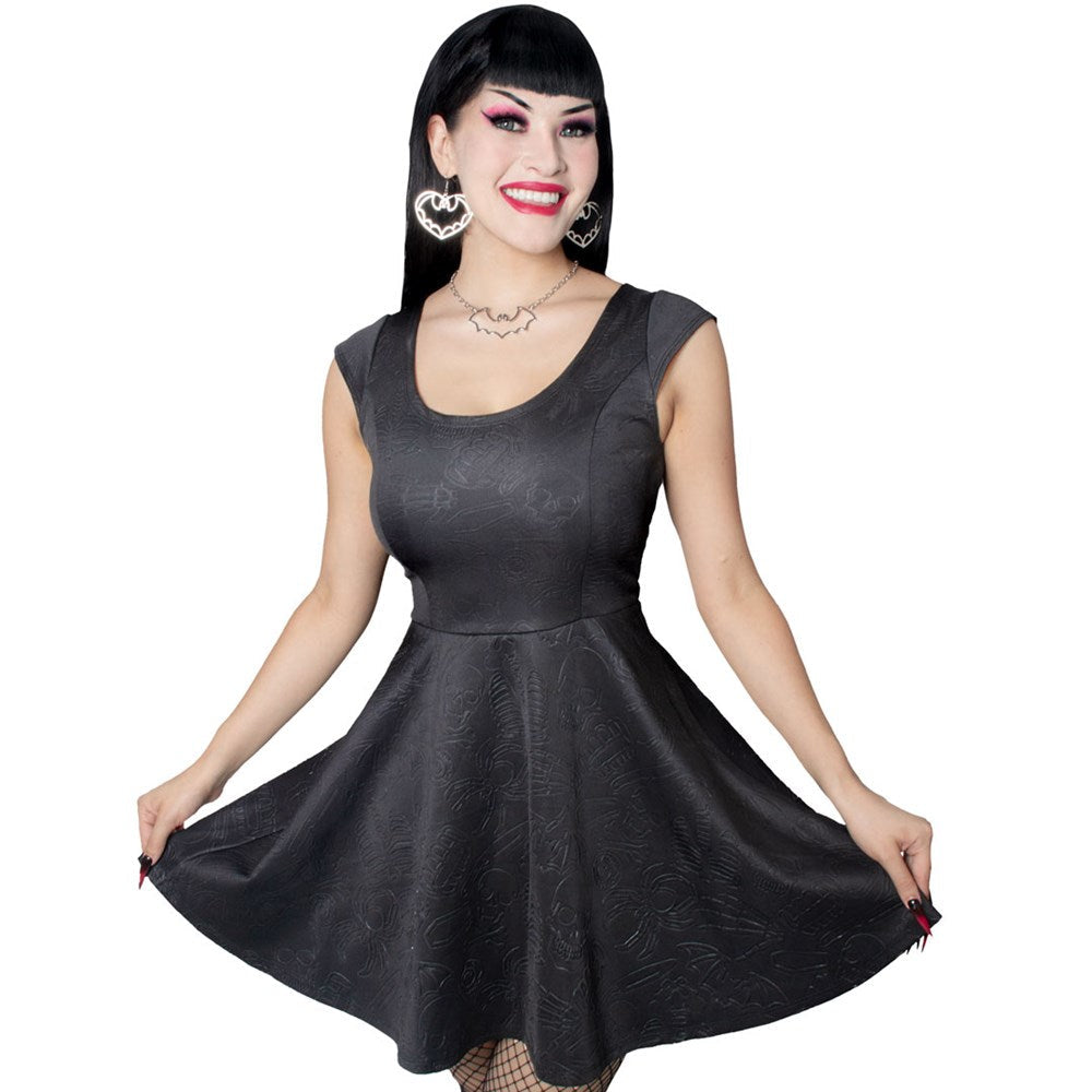Goth Woman wearing a black dress with embossed skulls, coffins and bats on a white background